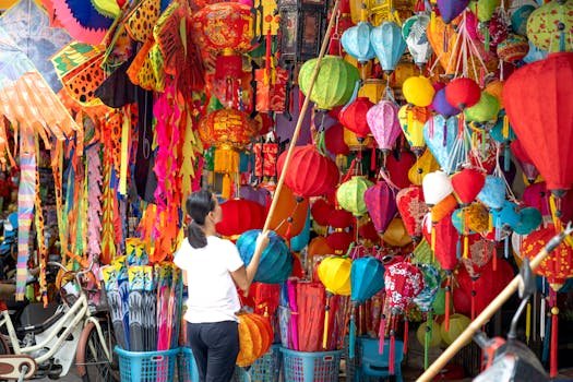 Anonymous local female vendor in casual clothes standing with colorful lanterns in street market with different traditional goods